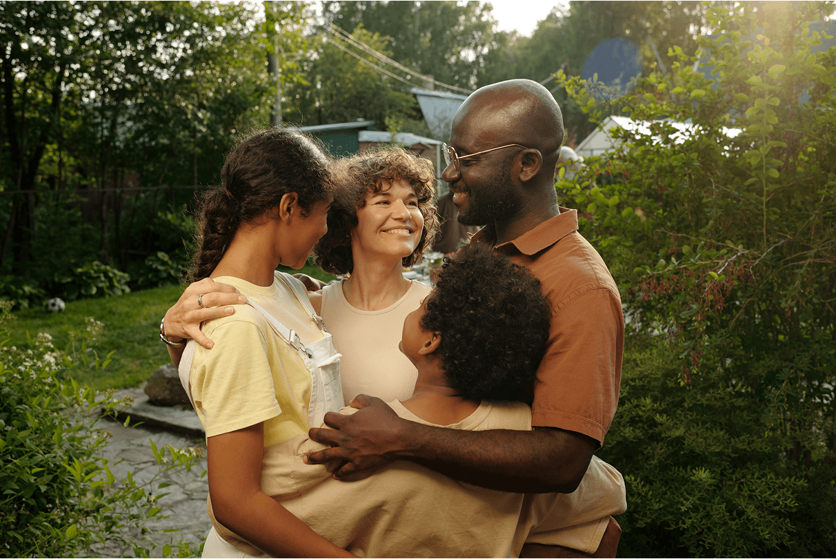 A family embraces together in a sunlit backyard.