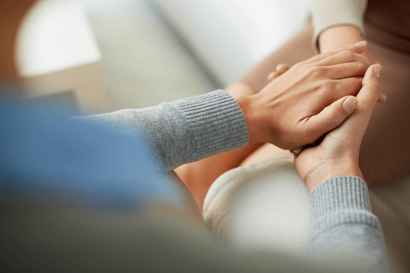 A caregiver holds a patient's hands in a quiet moment of comfort.