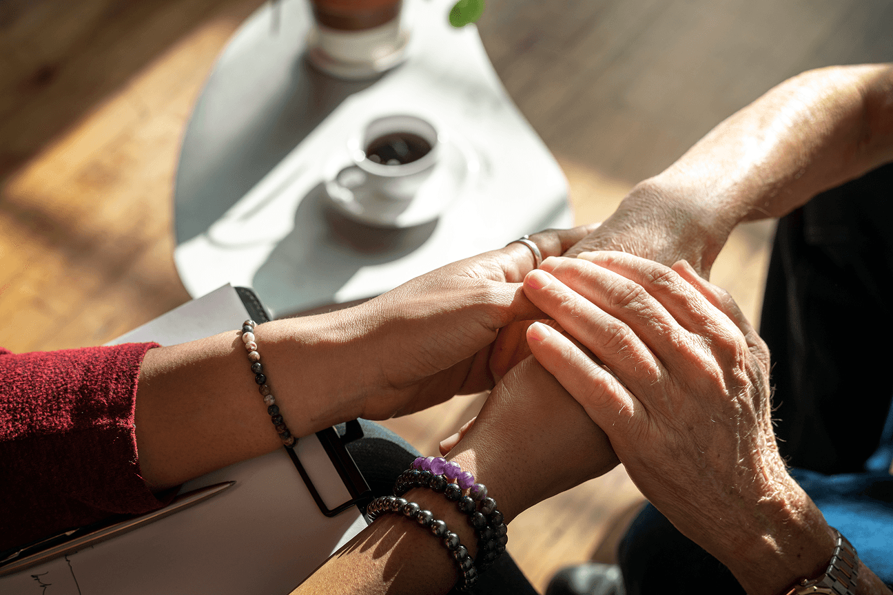 Two pairs of hands clasped together over a cafe table, wearing beaded bracelets.